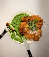 Fried chicken with green sauce on a plate with a fork and knife.